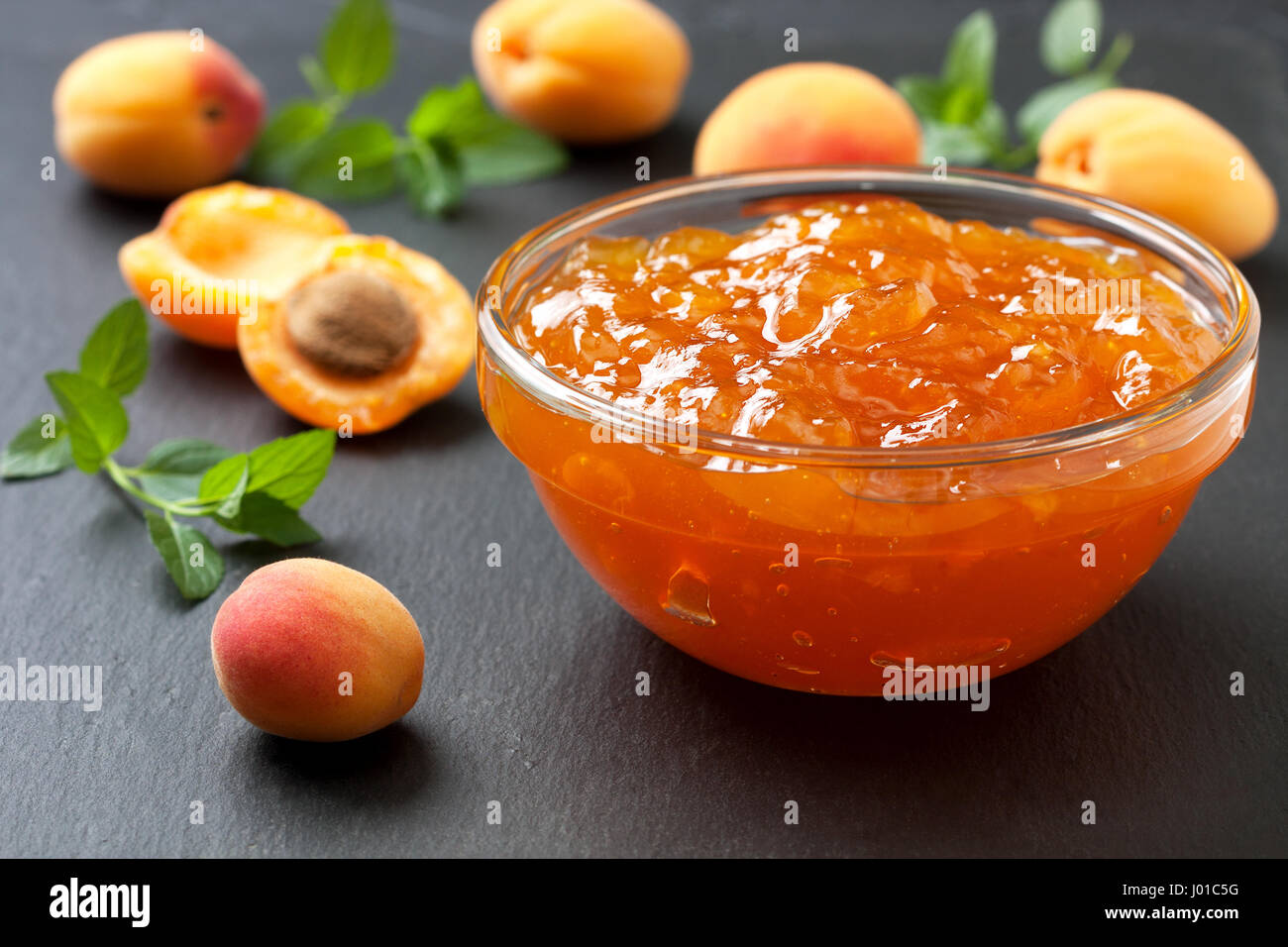 Confettura di albicocche in una ciotola di vetro , fresche Albicocche nero su sfondo di ardesia Foto Stock