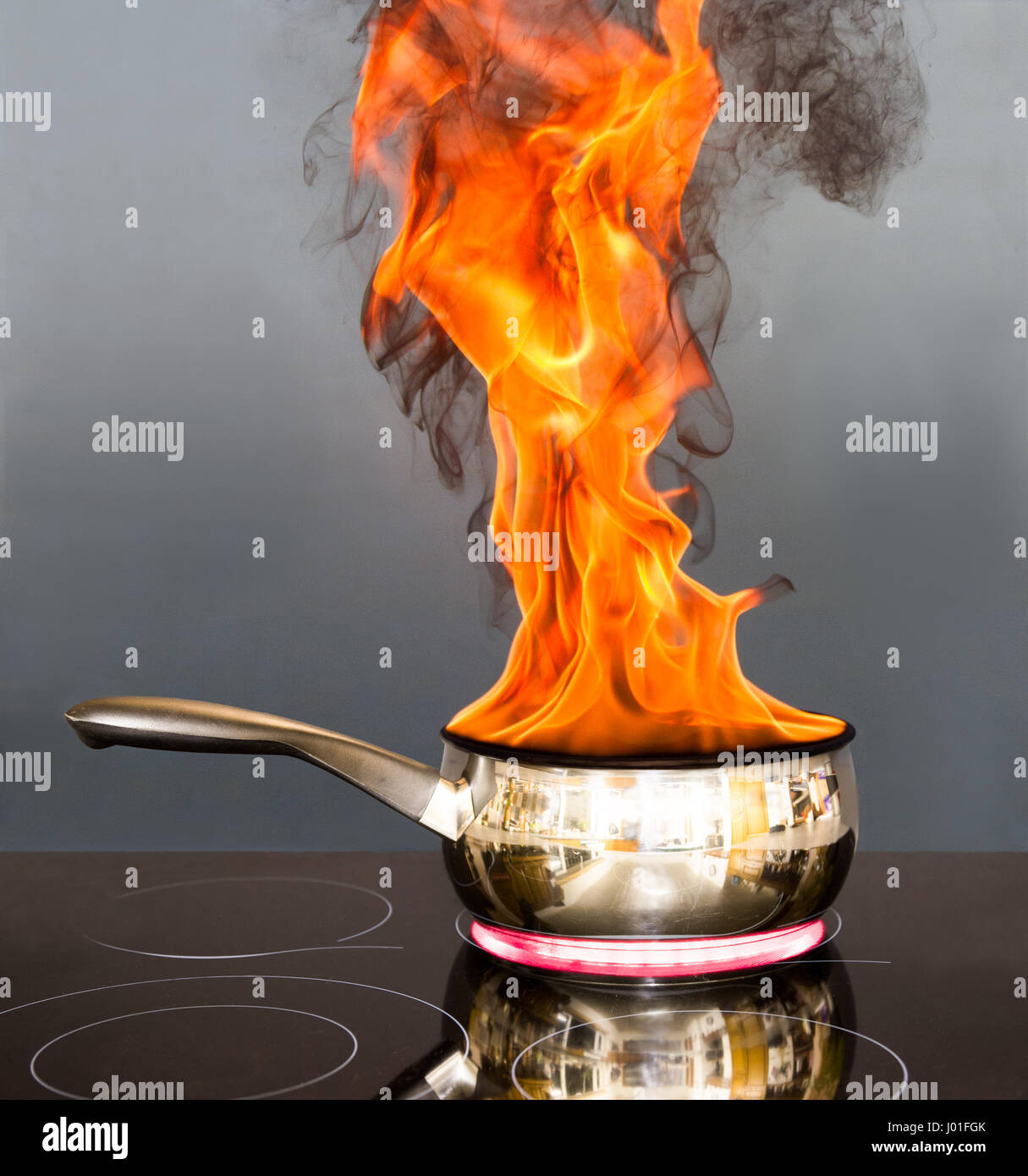 Pentola su un piano cottura con le fiamme che escono come un fuoco di teglia. Posizionate su un piano cottura elettrico su uno sfondo grigio. Foto Stock