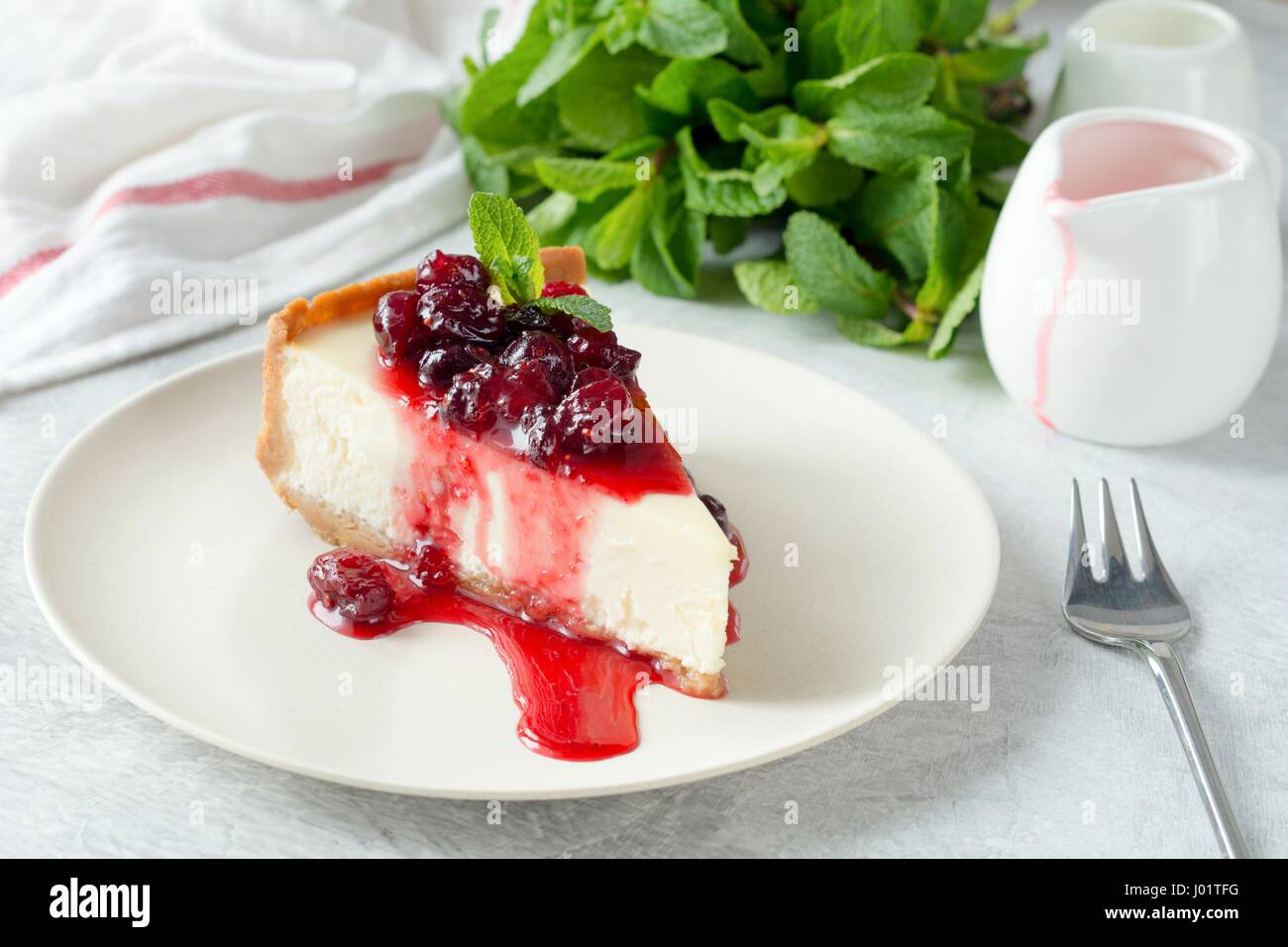 Fetta di cheesecake con ciliege acide e salsa di menta fresca sulla piastra bianca Foto Stock