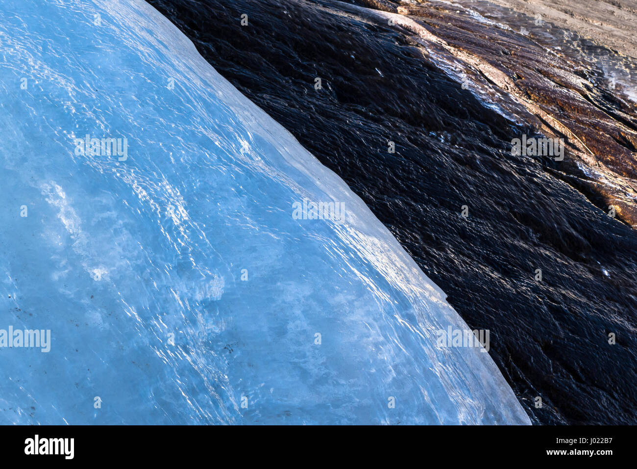 Rock parzialmente coperto dal ghiacciaio di fusione lentamente nella luce del sole Foto Stock