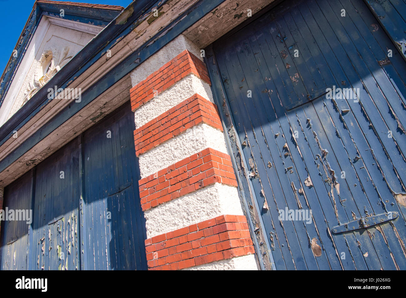 Squallido insiemi di garage o la fabbrica di porte in legno con peeling e sbiadita della vernice blu con il bianco e il rosso mattone colonne su un edificio vuoto in Avonmouth Foto Stock