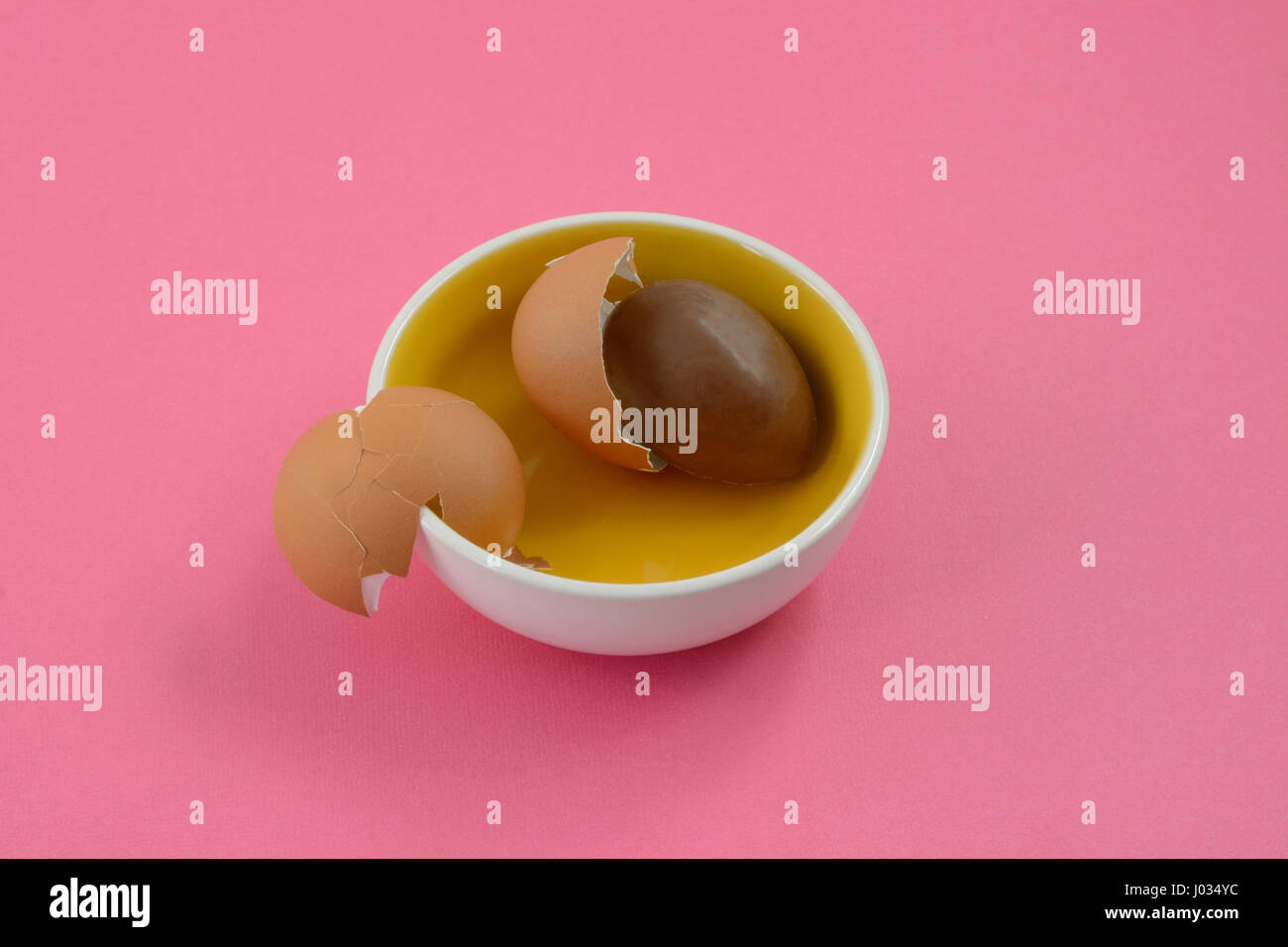 Il cioccolato uovo di Pasqua e le rotture di gusci delle uova all'interno piccolo vaso su sfondo rosa Foto Stock