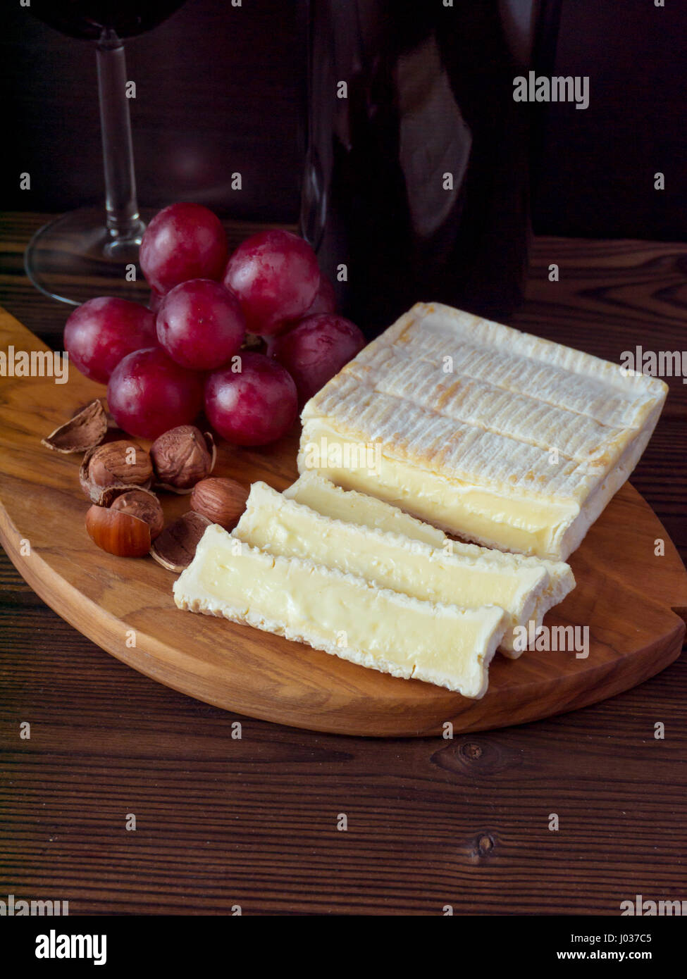 A forma di mattone di formaggio con muffa bianca, nocciole, rosso Uva e vino nel bicchiere e bottiglia Foto Stock