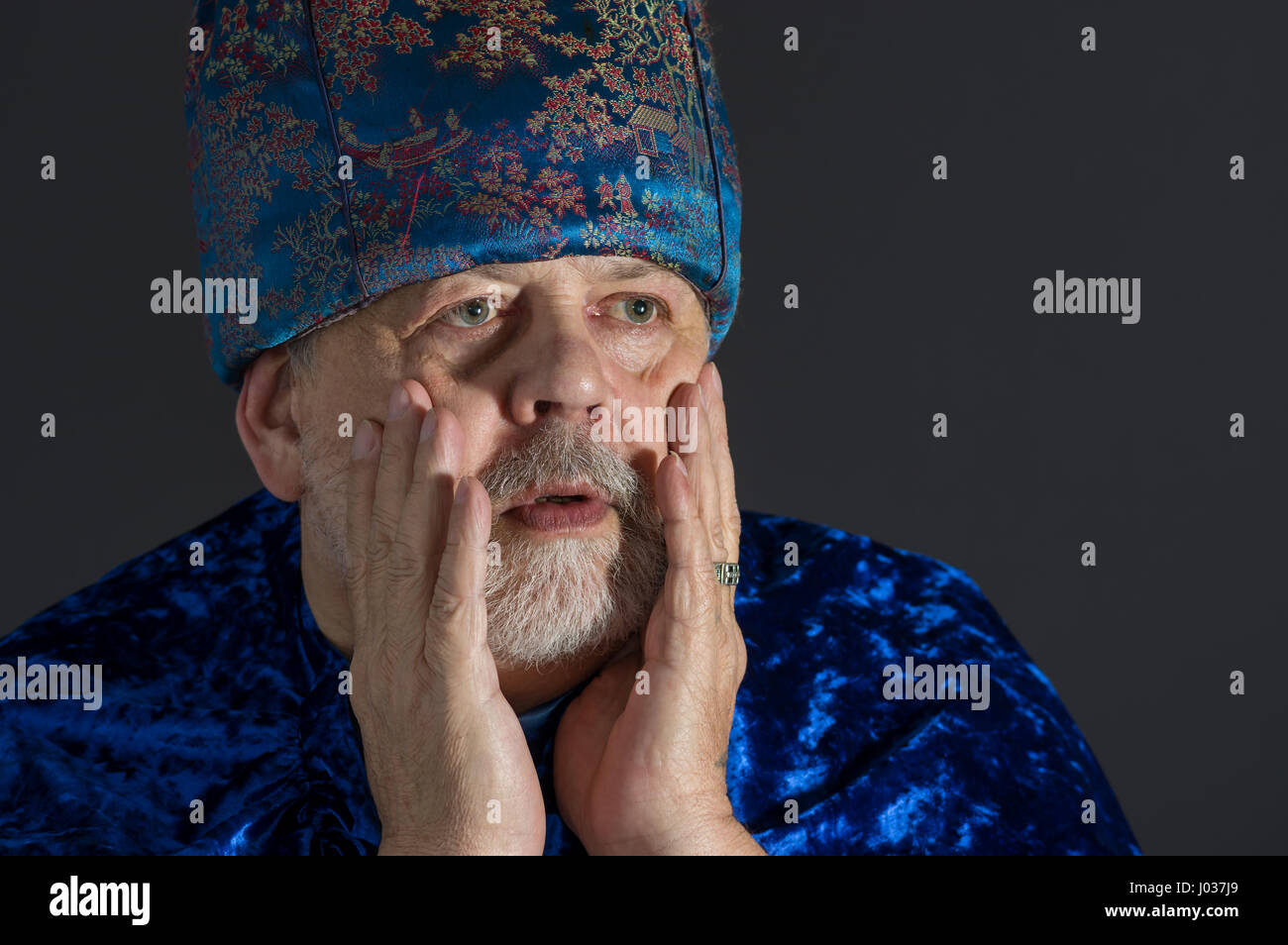 Ritratto di sollecite senior uomo in blu i vestiti orientali contro uno sfondo scuro Foto Stock