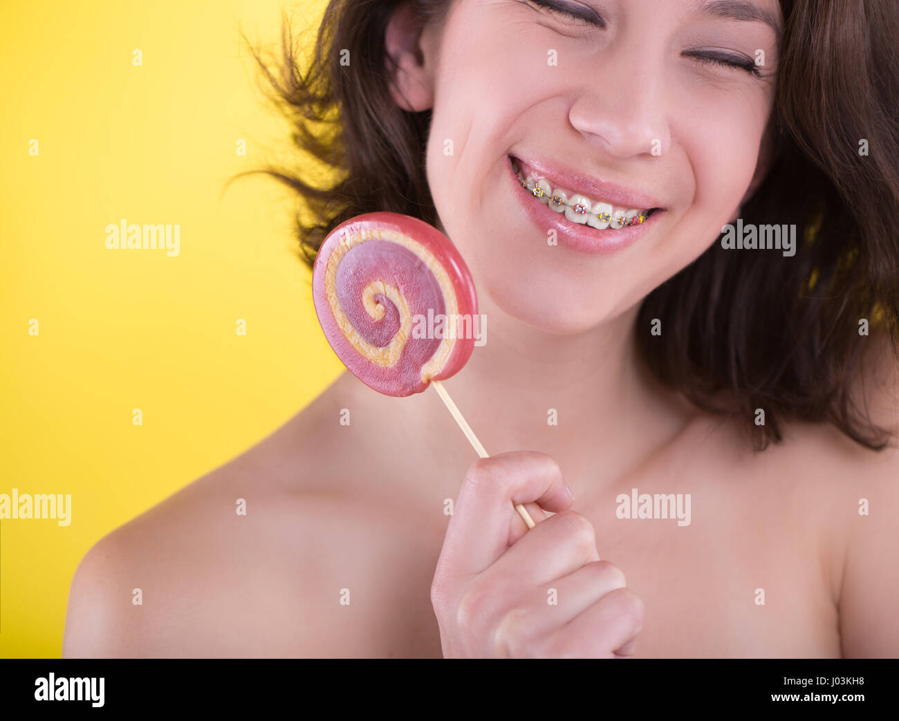 Giovane donna con multi-colore di staffaggio e candy in posa su sfondo giallo. Concetto dentale Foto Stock