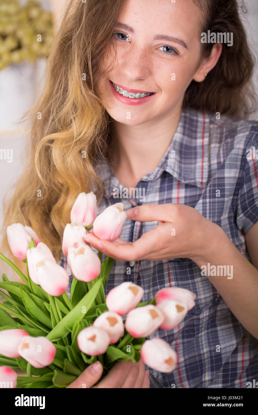 Una ragazza con bretelle in posa contro un muro di mattoni lo sfondo con un bouquet di tulipani. Concetto dentale Foto Stock