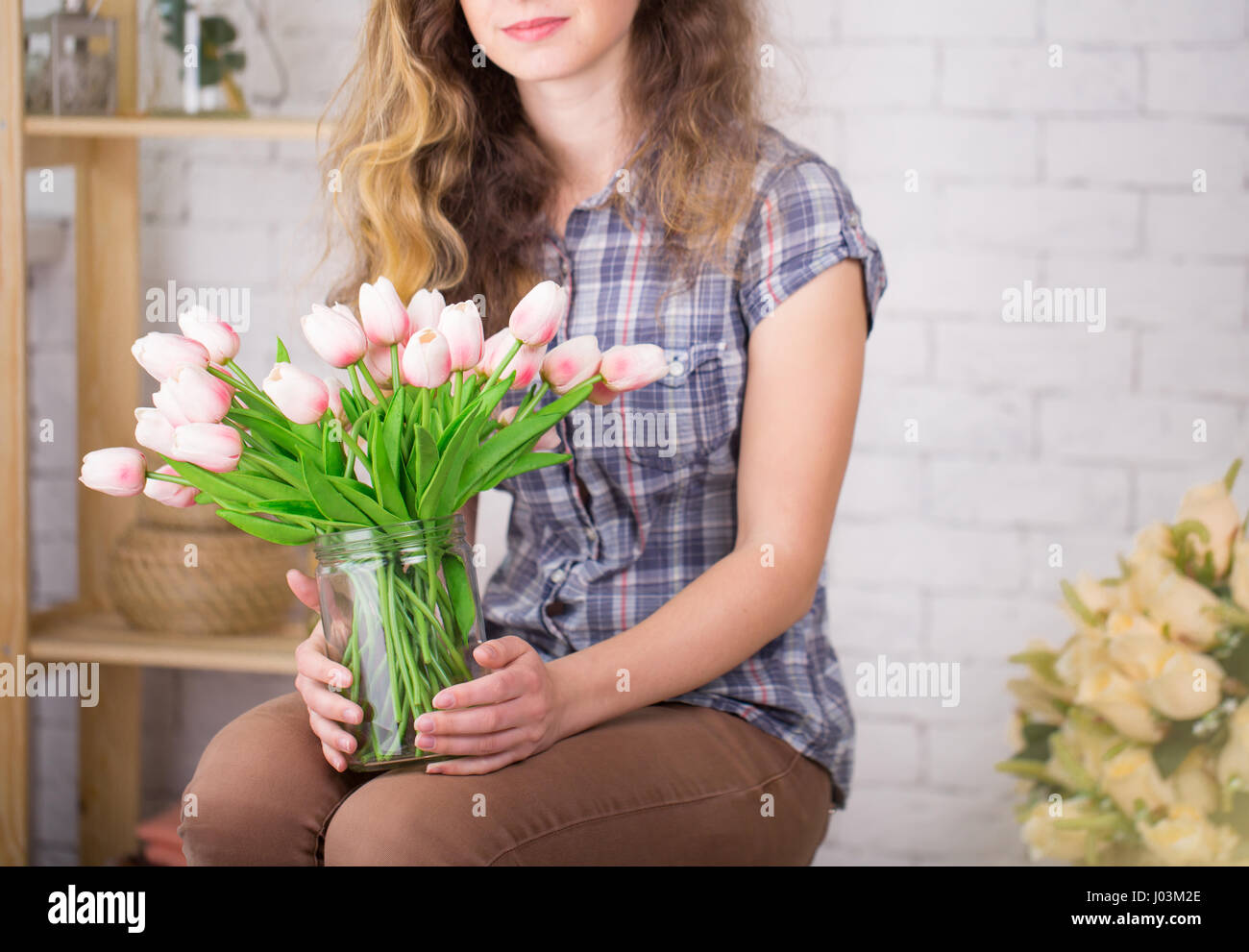 Una ragazza con bretelle in posa contro un muro di mattoni lo sfondo con un bouquet di tulipani. Concetto dentale Foto Stock