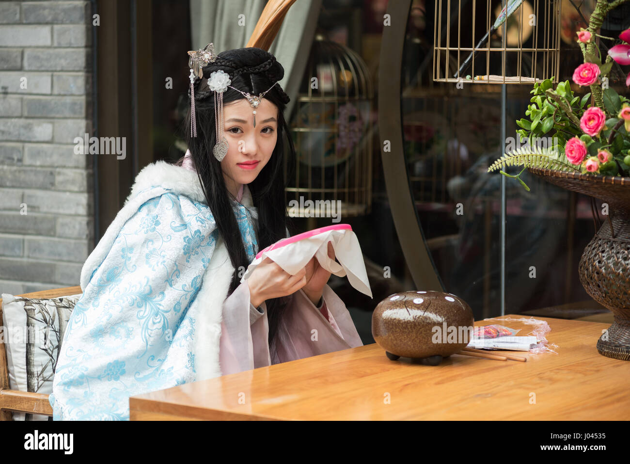 Chengdu, nella provincia di Sichuan, in Cina - Marte 25, 2017 : ragazza cinese di indossare abiti tradizionali a una tabella con un po' di tessitura tè in una strada. Foto Stock