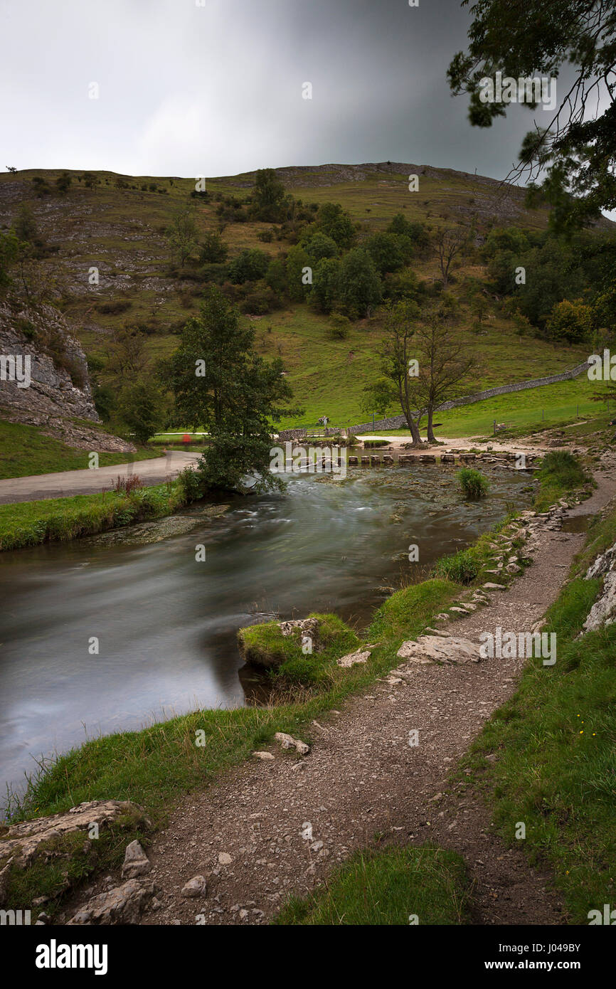 Una vista verso le pietre miliari sul fiume colomba nella Dovedale, Derbyshire. Lenta velocità shuuter offusca l'acqua e diversi blury shaddows di persone un Foto Stock