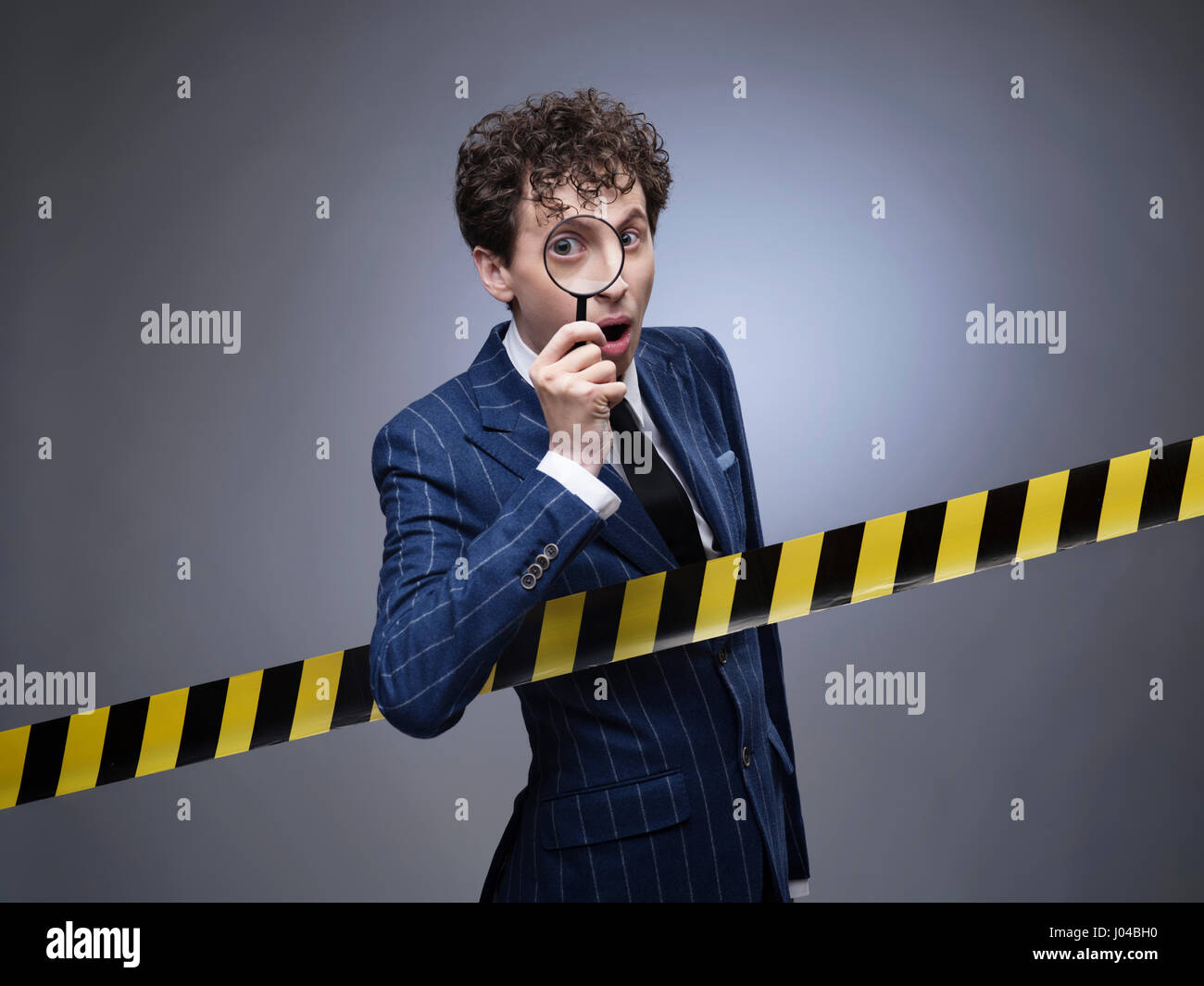 Funny Man con lente di ingrandimento si dipana il segreto attraverso la linea di polizia pericolo nastro. Foto Stock