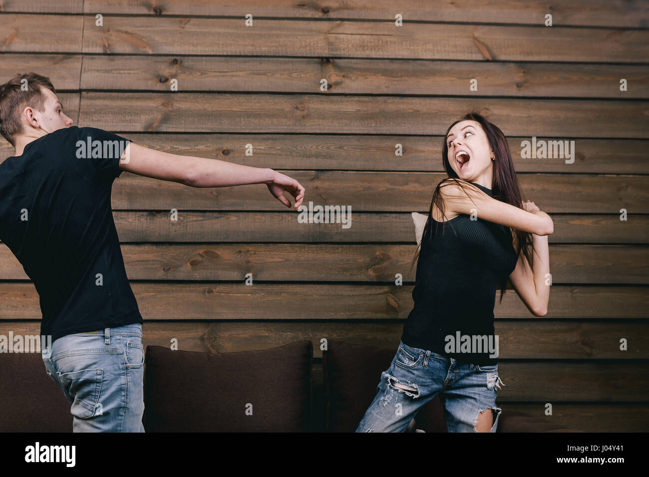 Allegro giovane avente pillow fight. Essi indossano in camicia nera e jeans e stand sulle ginocchia bendend sul letto. Chiunque è in possesso di un cuscino Foto Stock