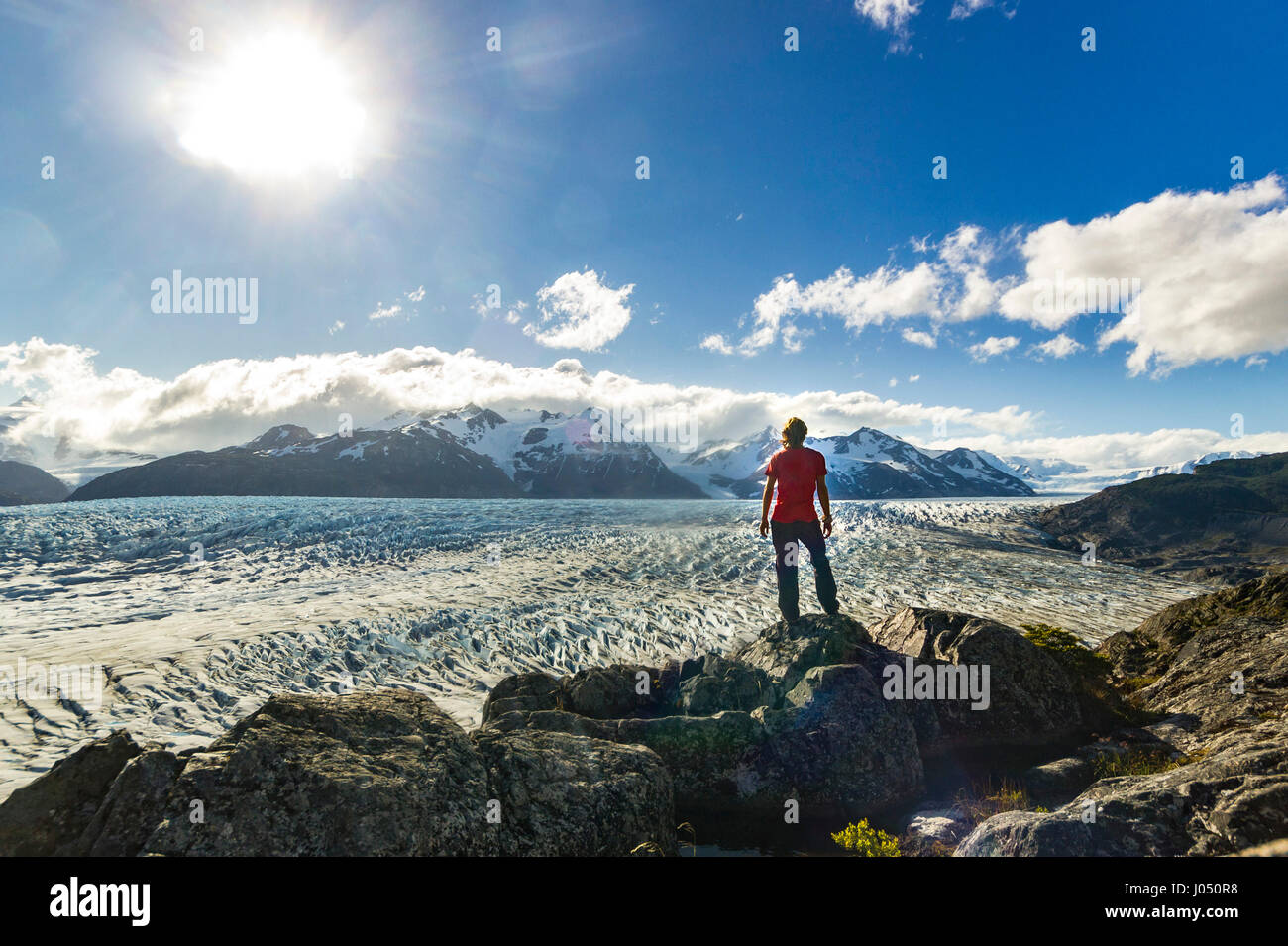 Uomo con der t-short in piedi sulla pietra sopra il ghiacciaio grigio in Patagonia al tramonto con il sole che splende Foto Stock