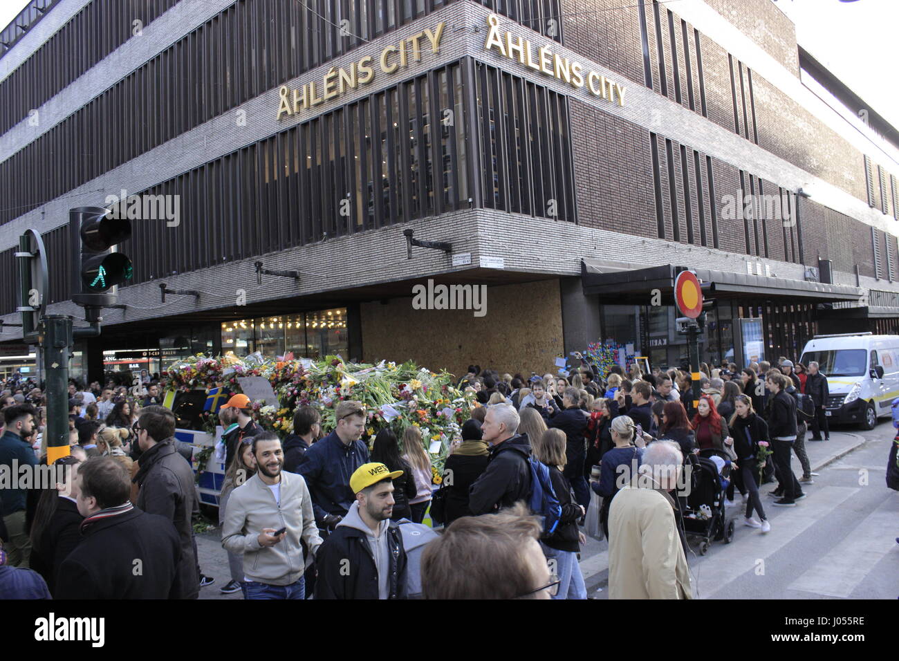 Folle si radunarono presso l'angolo di Drottninggatan & Master Samuelsgatan street, pieno di cui bouquet di fiori e dediche, dove il carrello utente malintenzionato terrorista ha concluso la sua mortale percorso di guida schiacciando la birra rubati carrello presso l'angolo dell'Ahlens city centre e dalla stazione della metropolitana (vedere la tavola di legno che copre il colpo posto all'angolo). La città di Stoccolma, Ahlens shopping centre, Svezia. 9 aprile 2017. Foto Stock