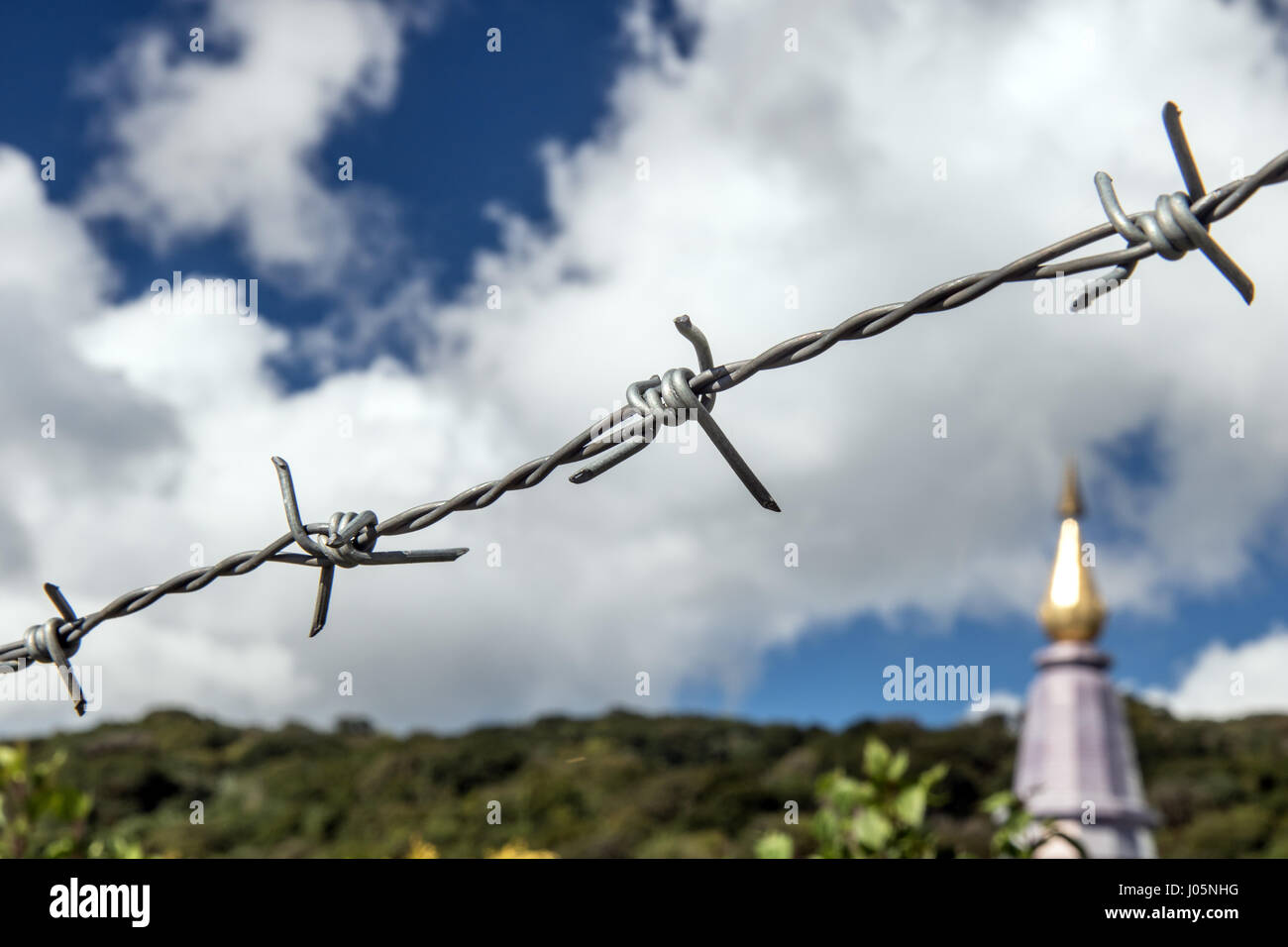 Dettaglio di un recinto per proteggere il monastero buddista sulla Montagna Doi Inthanon.Il filo spinato vicino. Filo trafilato recinto sotto il cielo blu. Foto Stock