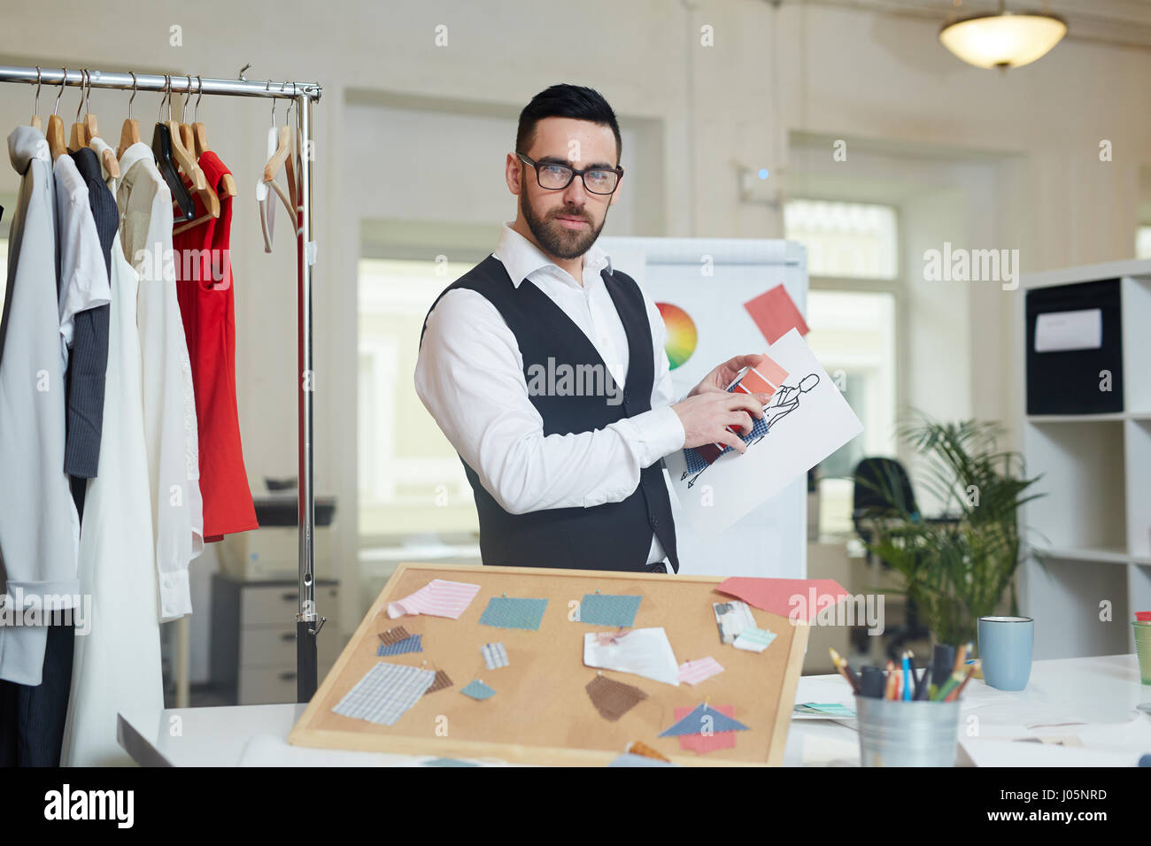 Sarta con il disegno e la tavolozza dei colori in piedi dal suo posto di lavoro nella sartoria studio Foto Stock