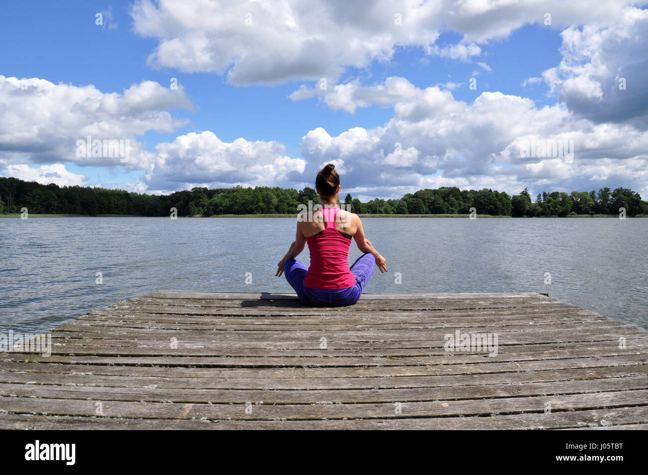 Giovane donna attiva fare yoga posizioni sul molo in legno sulla riva del lago in polacco countsydie nella regione Mazury Foto Stock