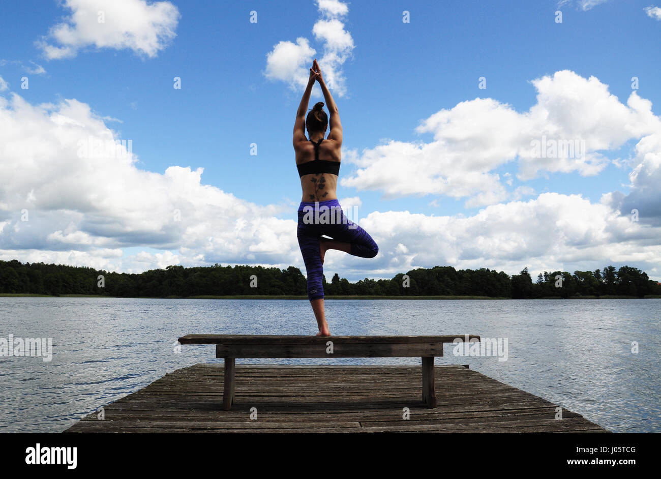 Giovane donna attiva fare yoga posizioni sul molo in legno sulla riva del lago in polacco countsydie nella regione Mazury Foto Stock