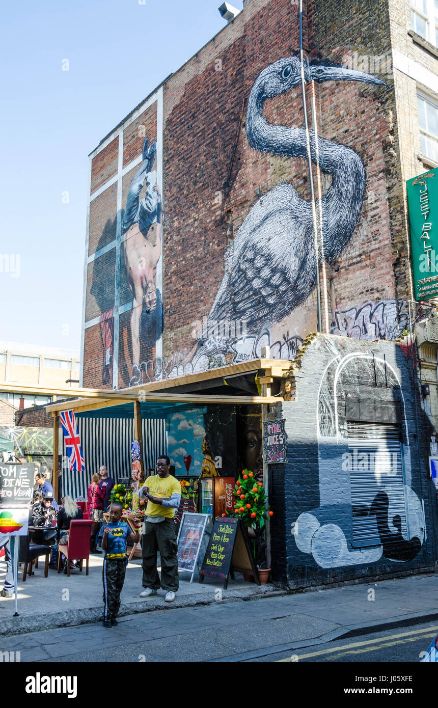 Etiope cucina vegana bancarelle su Hanbury Street appena fuori la Brick Lane nella zona est di Londra. Al di sopra è una grande arte di strada della verniciatura di un airone. Foto Stock