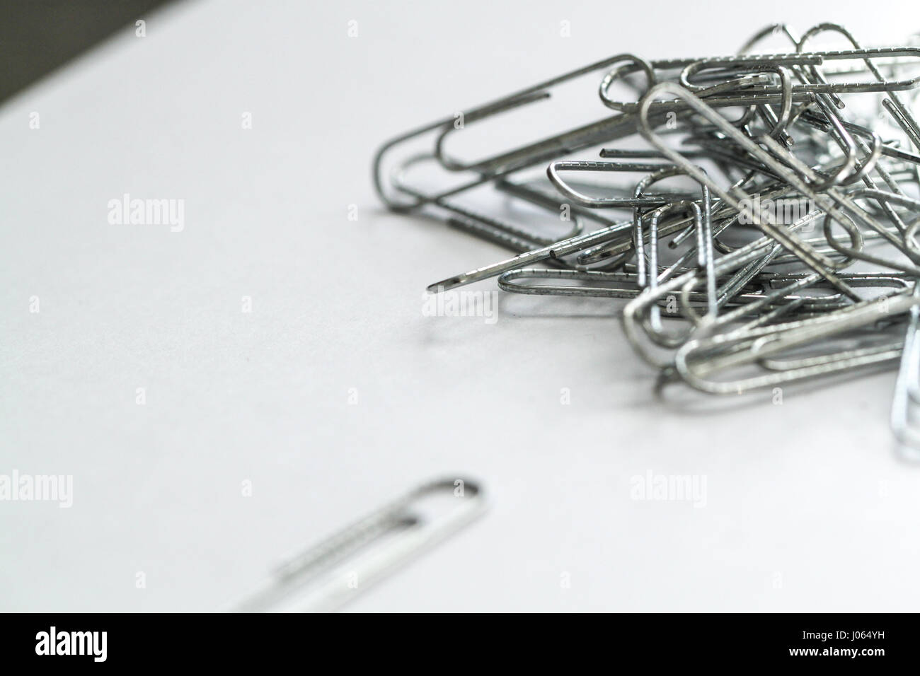 Primo piano di una pila confusa di argento filo metallico graffette con un singolo clip di carta in primo piano. Foto Stock