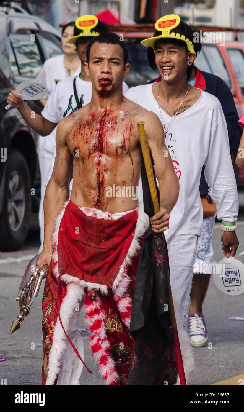 Un macchiate di sangue uomo cammina per le strade. Rifatti gli occhi con probabilmente il più hardcore gruppo di vegetariani si sono mai probabilità di vedere. Le spettacolari colpi di sangue tinto uomini mostrare loro perforazione coraggiosamente il loro guance con una varietà di oggetti appuntiti come ad esempio spiedini, grandi coltelli e aghi da maglia. Altre immagini mostrano gli uomini costringendo a più voci straordinarie attraverso la loro bocca compreso ombrelloni e un uomo anche la gestione per ottenere un intero pala attraverso le sue guance. L annuale Phuket Vegetarian Festival si svolge nel mese di ottobre. Foto Stock