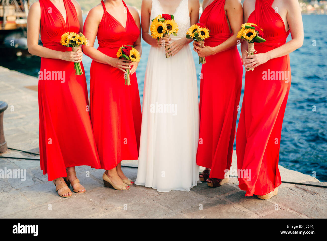 Damigelle in abiti rossi, nelle mani di mazzi di fiori di girasole.  Sposarsi sul mare in Montenegro Foto stock - Alamy