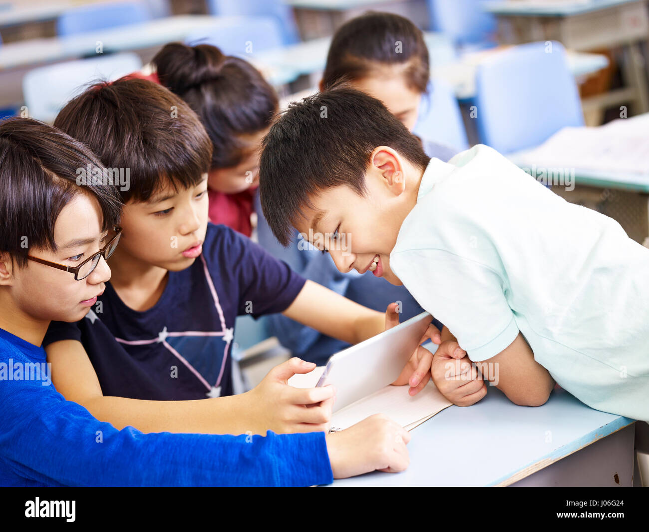 Gruppo asiatico scolari elementari usando tavoletta digitale insieme in aula. Foto Stock