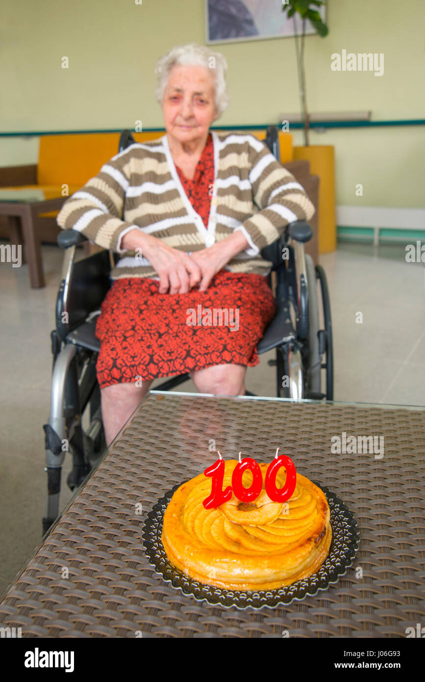 Vecchia donna in una casa di cura, su di lei un centinaio di compleanno con la sua festa di compleanno torta del. Foto Stock