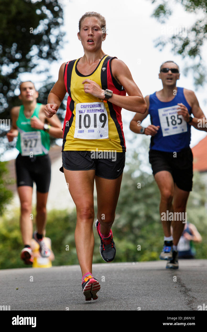 Una giovane donna / donna atleta che indossa in esecuzione abbigliamento sportivo è raffigurato in esecuzione in una mezza maratona corsa su strada in Chippenham, England, Regno Unito Foto Stock