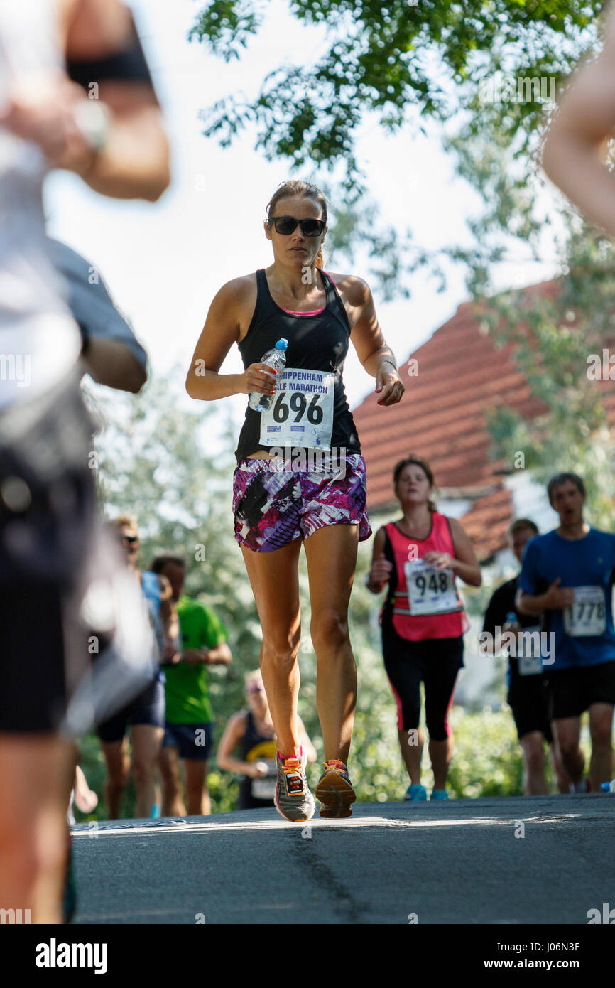 Una giovane donna / donna atleta che indossa in esecuzione abbigliamento sportivo è raffigurato in esecuzione in una mezza maratona corsa su strada in Chippenham, England, Regno Unito Foto Stock