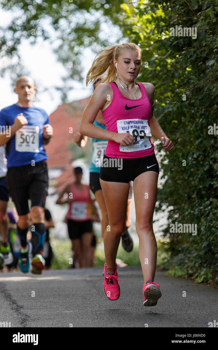 Una giovane donna / donna atleta che indossa in esecuzione abbigliamento sportivo è raffigurato in esecuzione in una mezza maratona corsa su strada in Chippenham, England, Regno Unito Foto Stock