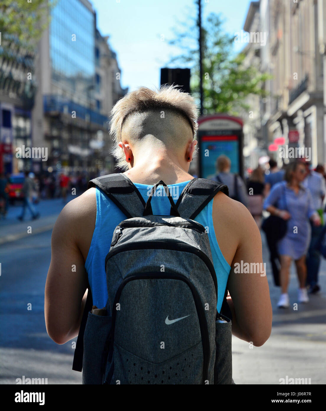 Giovane uomo rasato con retro e lati indossando un nike back pack utilizzando il suo smartphone Foto Stock