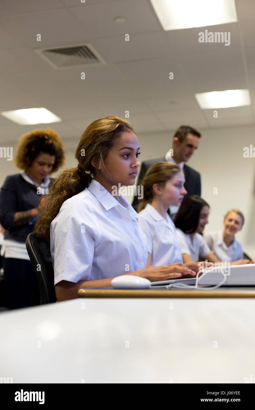 Studenti di lavorare su computer a scuola. Gli insegnanti possono essere visti al di fuori della messa a fuoco in background. Foto Stock