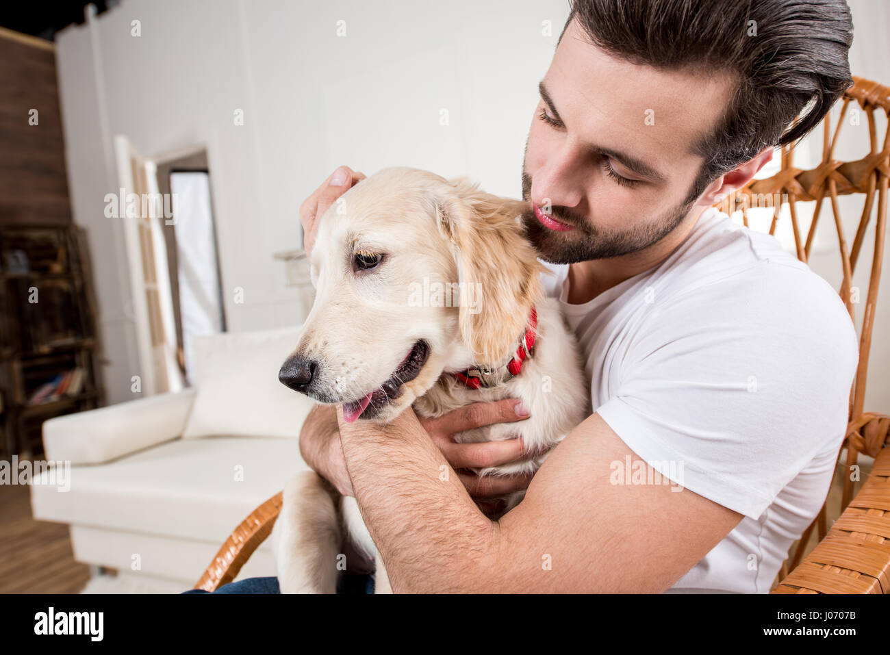 Giovane uomo seduto nella sedia a dondolo e azienda carino golden retriever cucciolo Foto Stock