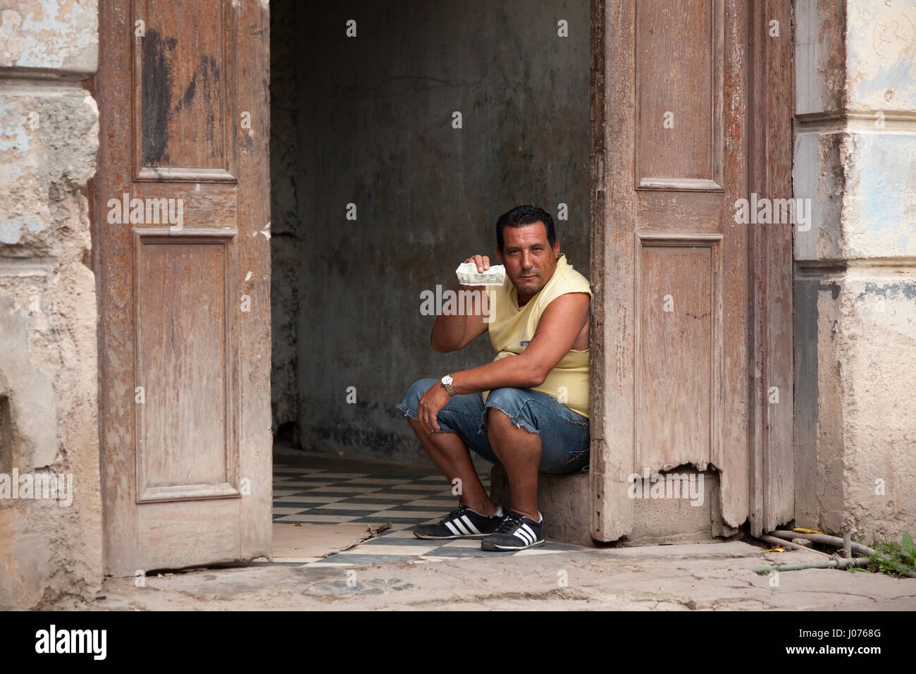 Un uomo con un peso cubano seduto all'interno di un palazzo della vecchia Havana, Cuba. Foto Stock