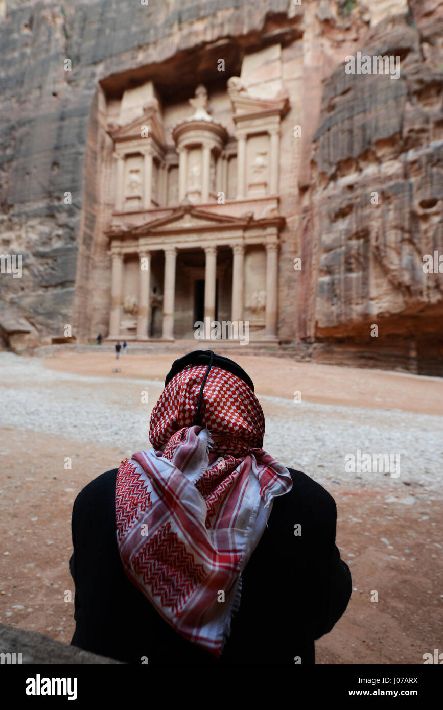 Un beduino uomo seduto dal Tesoro rocce scolpite tomba nella città antica di Petra, Giordania. Foto Stock