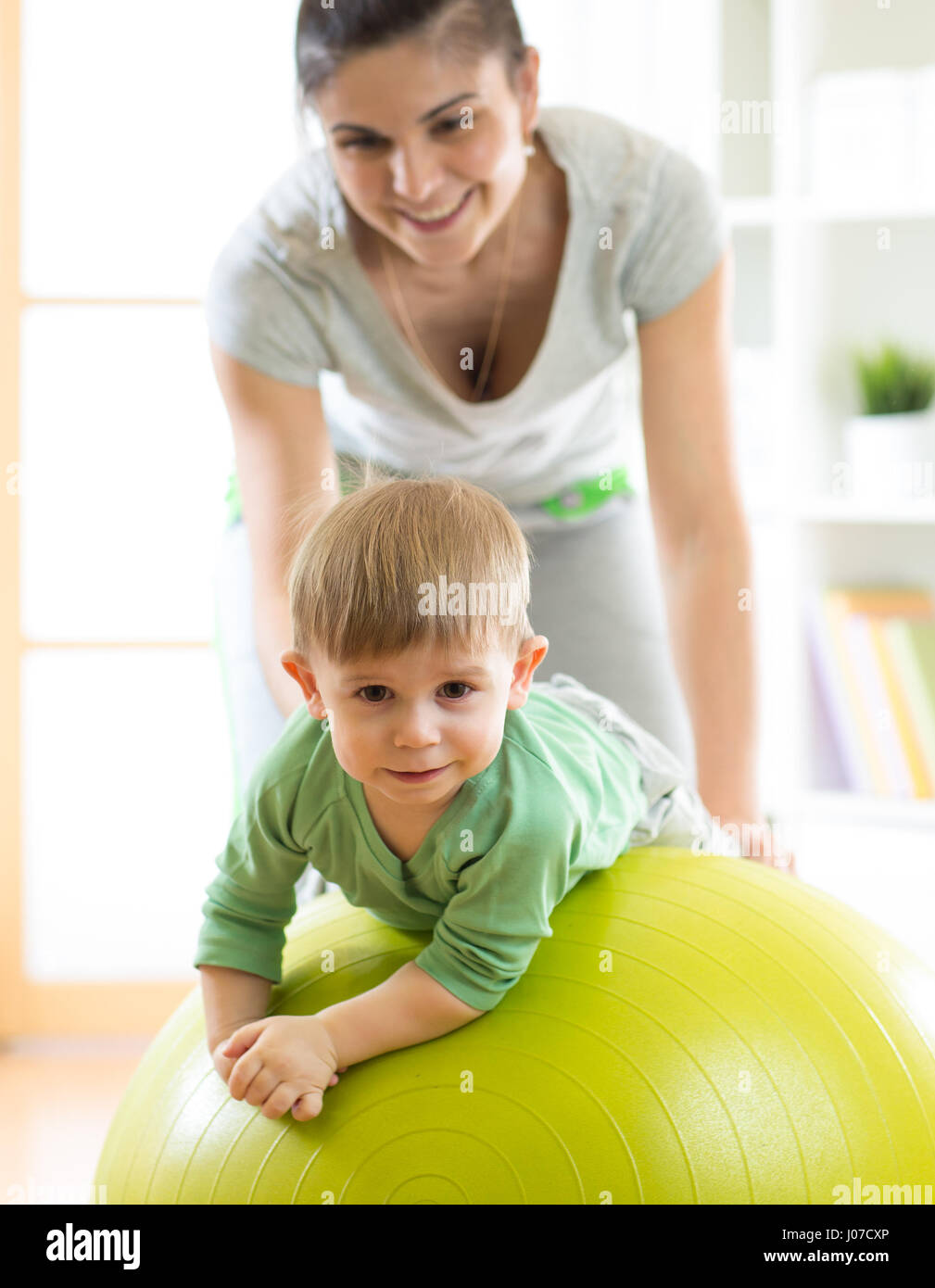Il bambino gioca con la palla ginnica con la madre a casa Foto Stock