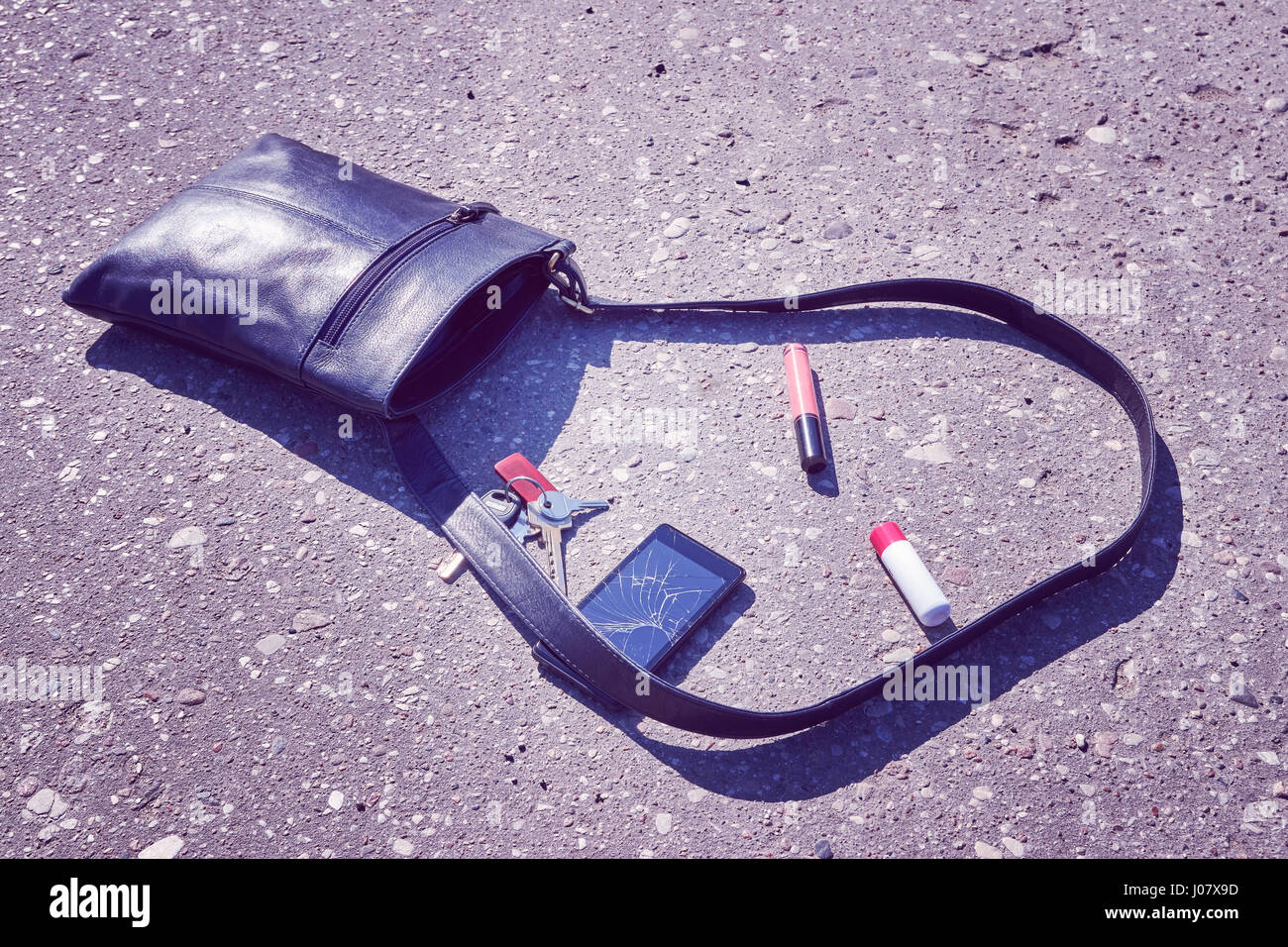 Borsetta, telefono cellulare con schermo rotto, le chiavi e il rossetto sulla strada asfaltata, quadro concettuale, tonificazione del colore applicato. Foto Stock