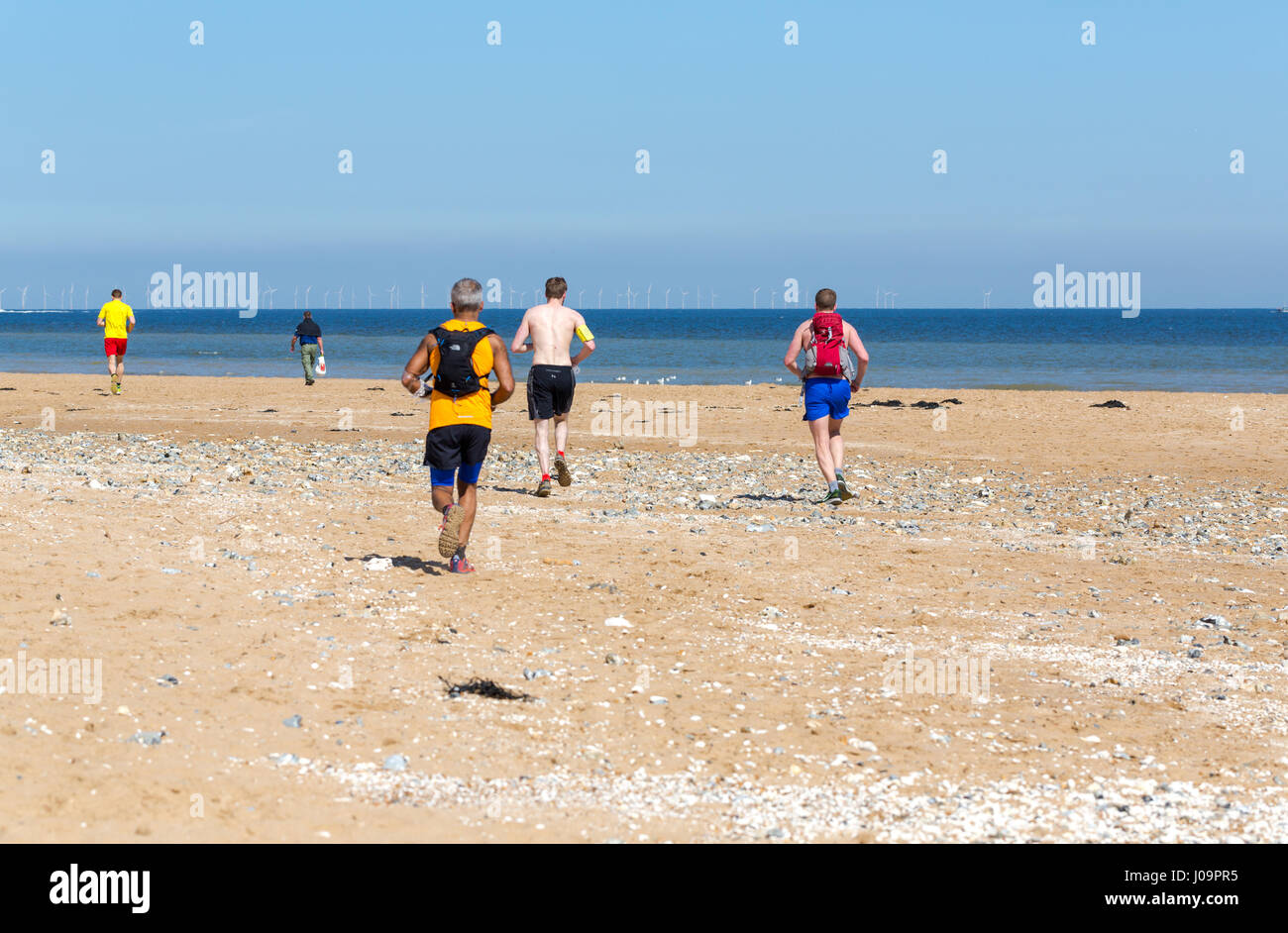Gruppo reali di giovani uomini e donne correre sulla spiaggia a Margate, Kent, Inghilterra Foto Stock