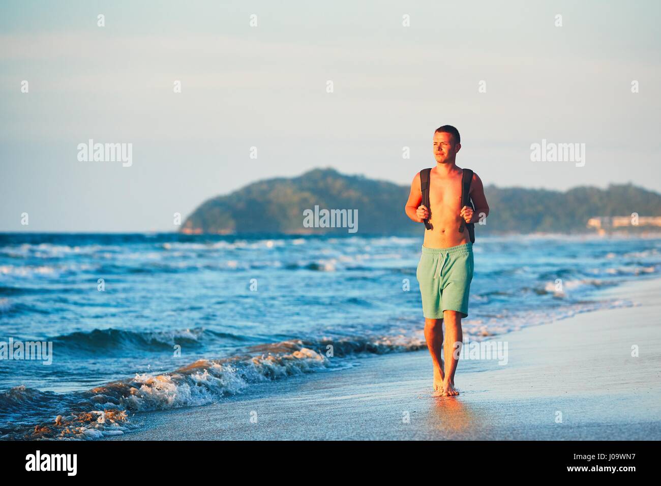 Giovane uomo con zaino camminando sulla bellissima spiaggia. Foto Stock