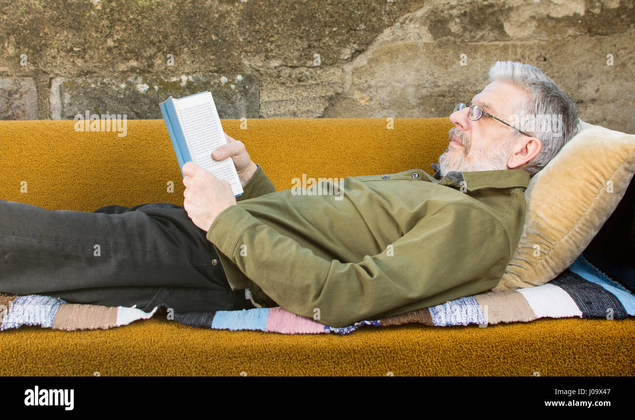 Senior uomo leggendo un libro in divano letto nel cortile posteriore Foto Stock
