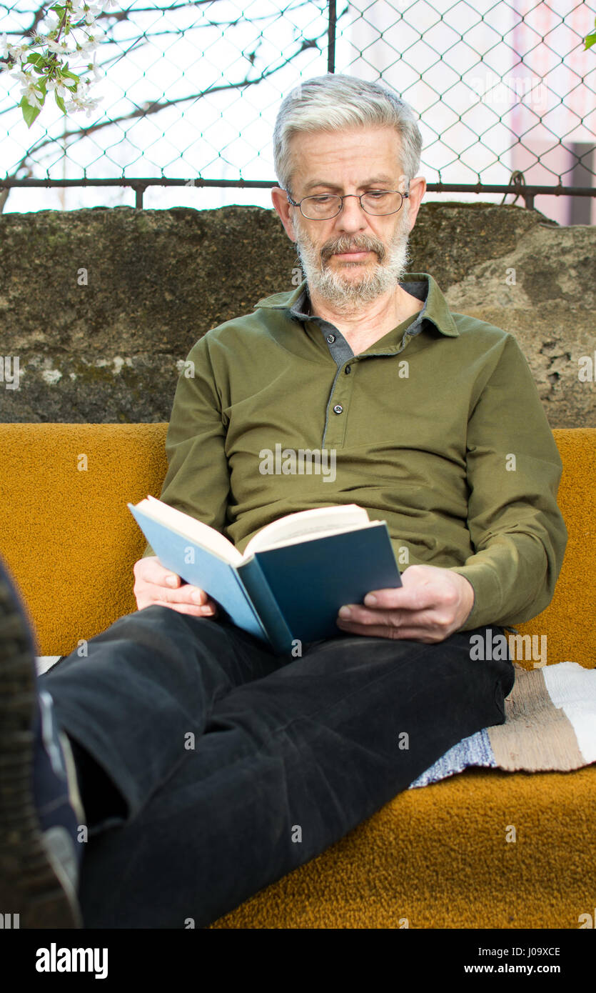 Senior uomo leggendo un libro in divano letto nel cortile posteriore Foto Stock