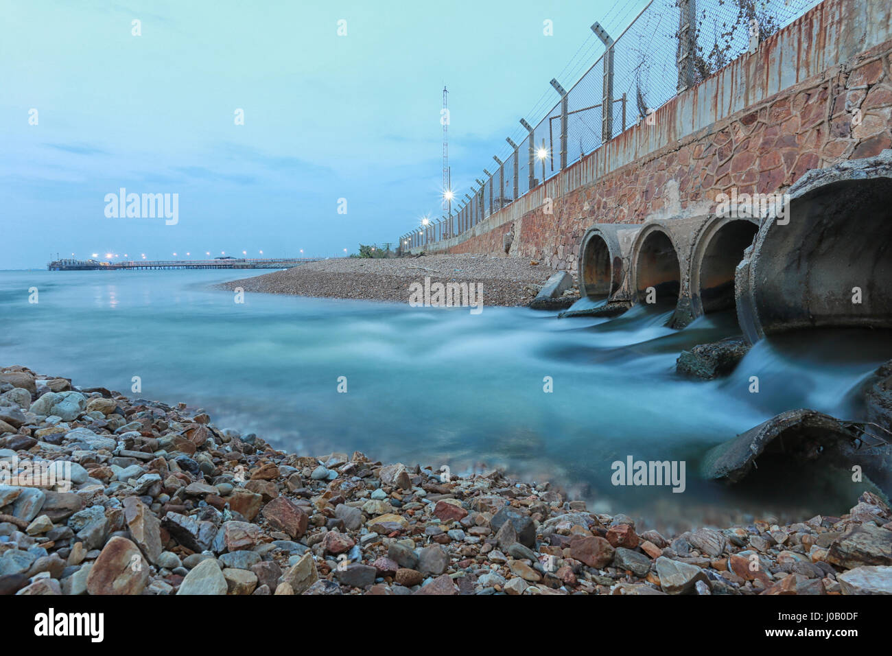 Il tubo drenante con acqua che scorre in mare la sera. Foto Stock