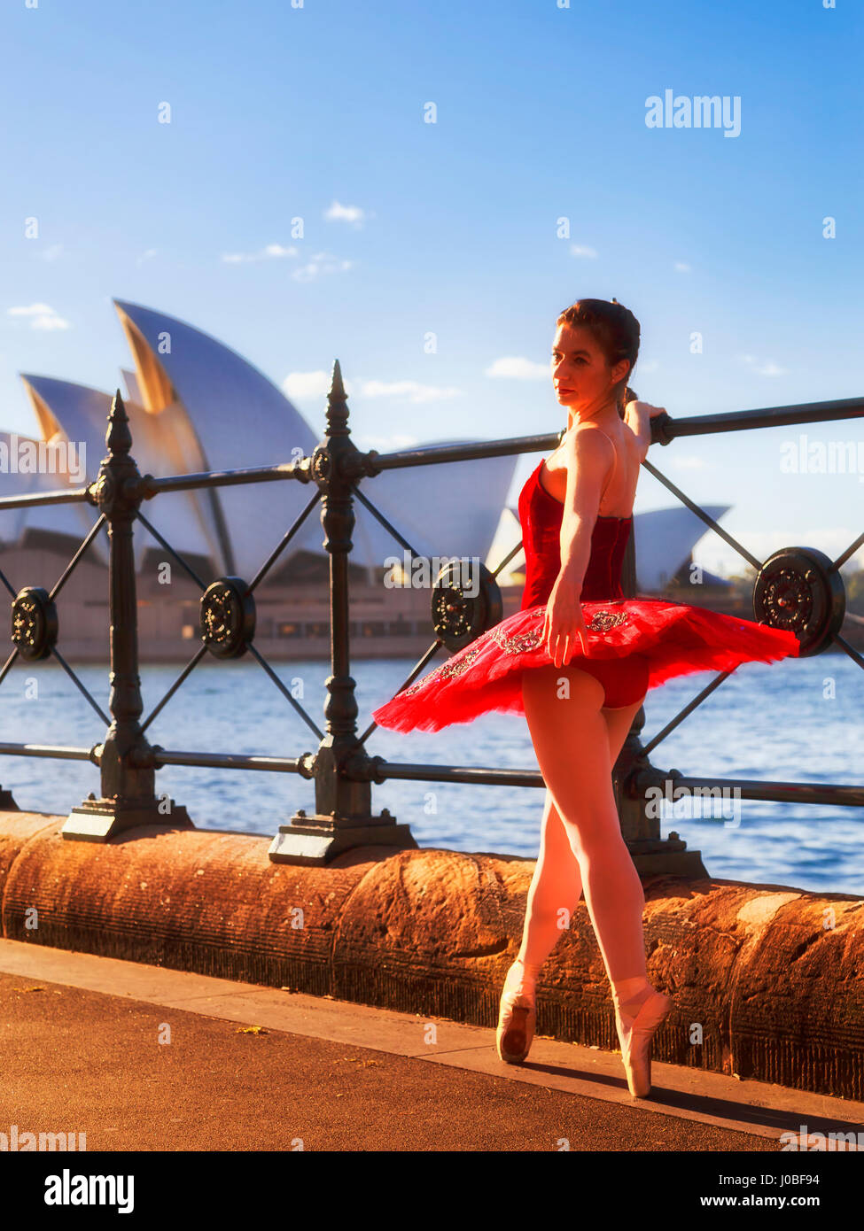 Street dance di eseguire la ballerina in rosso concerto Tutu in ballo nel punto scarpe in un recinto di Sydney Harbour in caldi raggi del sole di mattina. Foto Stock