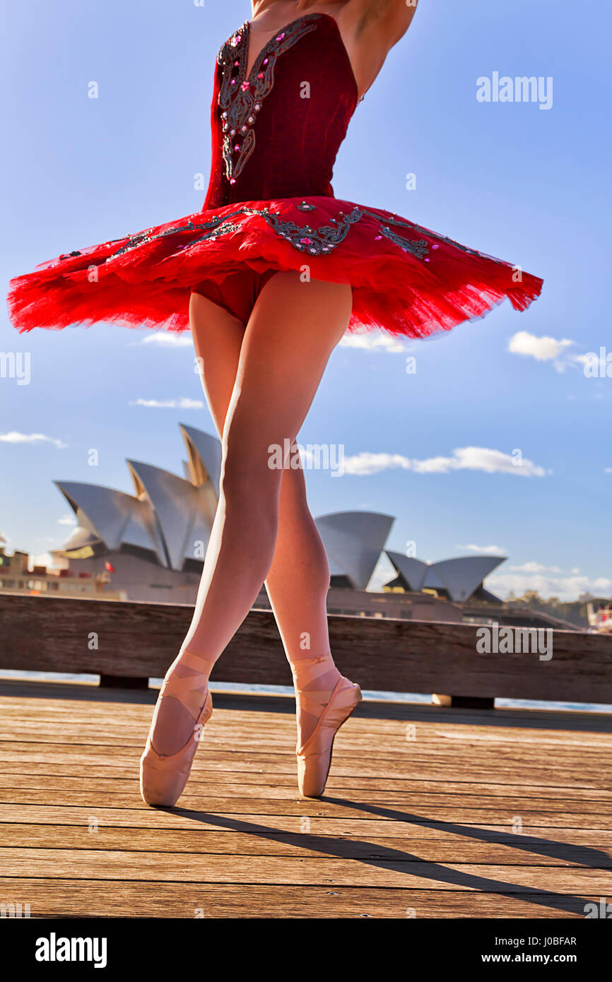 Ballerina femmina in concerto Tutu rosso stretching sui punti all'aperto di Sydney sotto il caldo sole di luce. Street ballet dancing sulla passerella di legno contro b Foto Stock