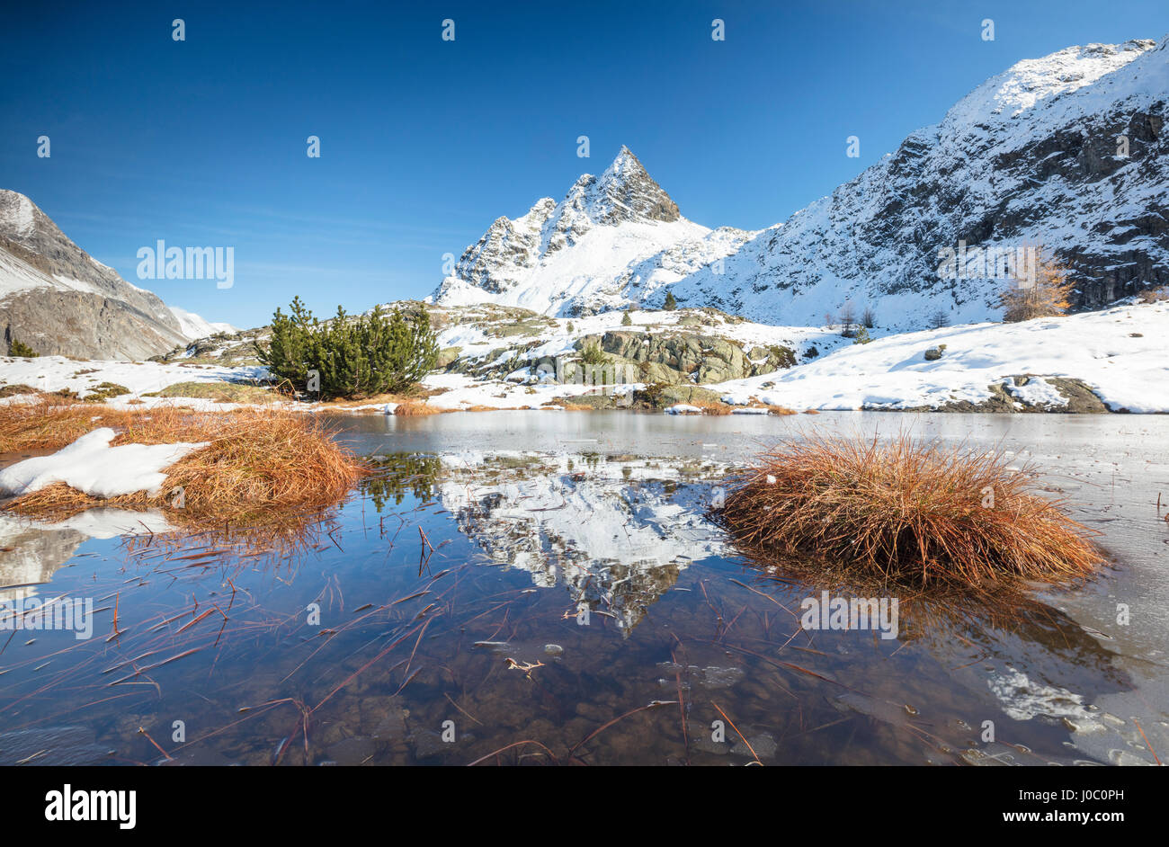 Vette innevate sono riflesse nel lago alpino parzialmente congelato, Lejets Crap Alv del Cantone dei Grigioni, Engadina, Svizzera Foto Stock