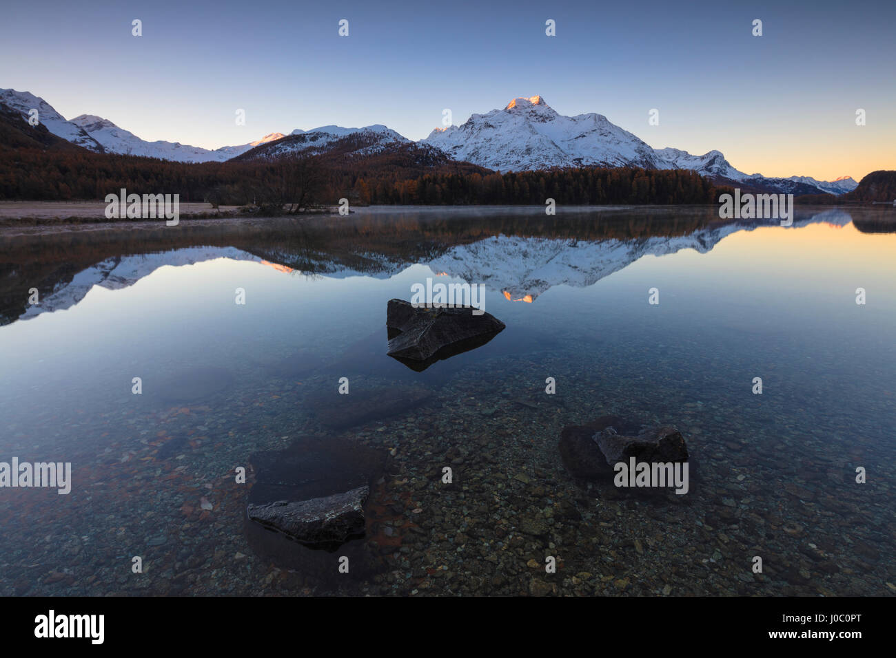 Le cime innevate sono riflesse nel lago a smusso sunrise, St Moritz, Canton Grigioni, Engadina, Svizzera Foto Stock