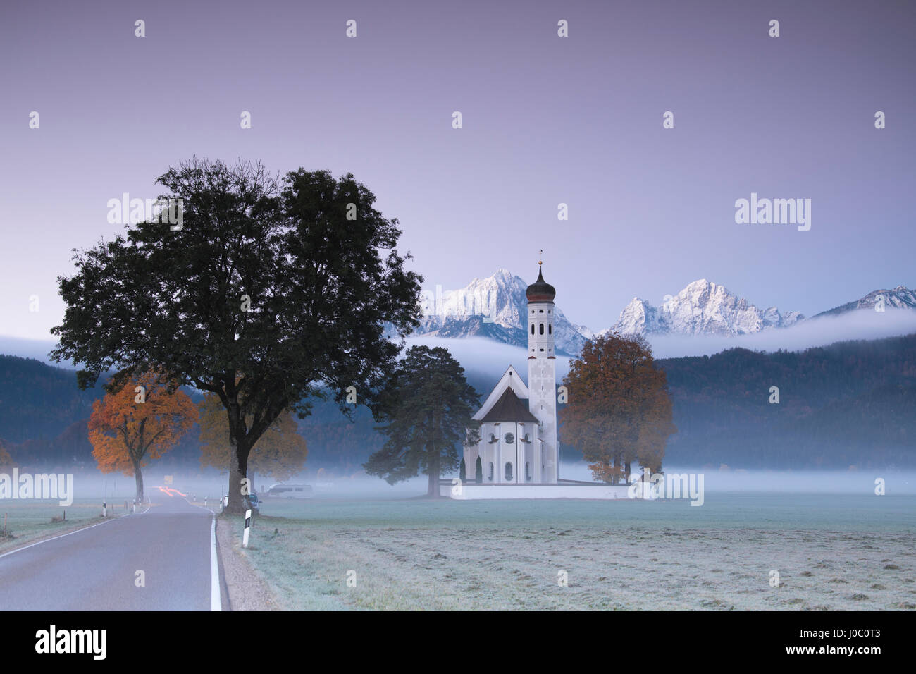 Pink sunrise e la nebbia di autunno a San Coloman Chiesa incorniciata da vette innevate, Schwangau, Baviera, Germania Foto Stock