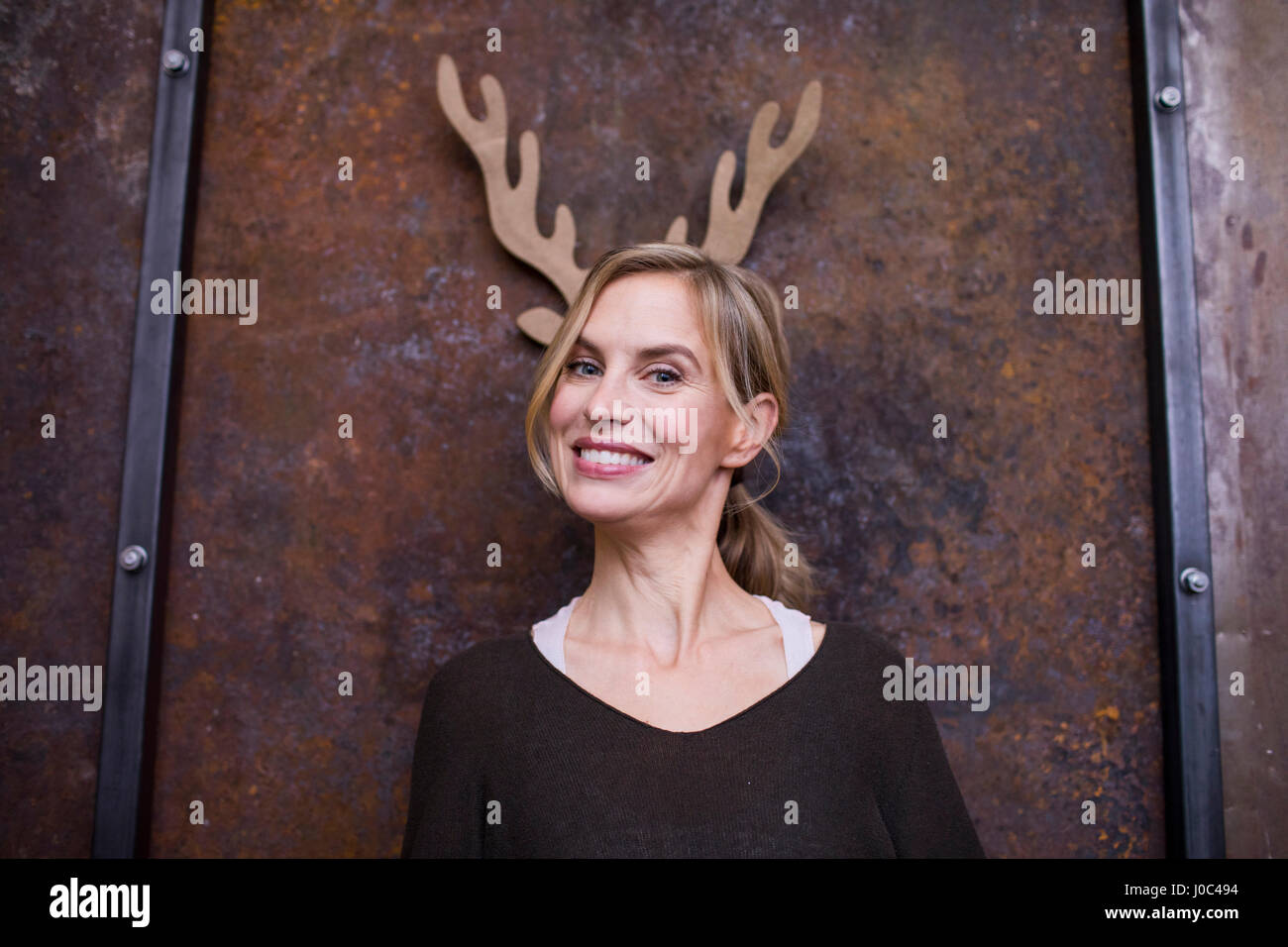 Ritratto di metà donna adulta, sorridente, cartone corna di renne sulla parete dietro di lei Foto Stock