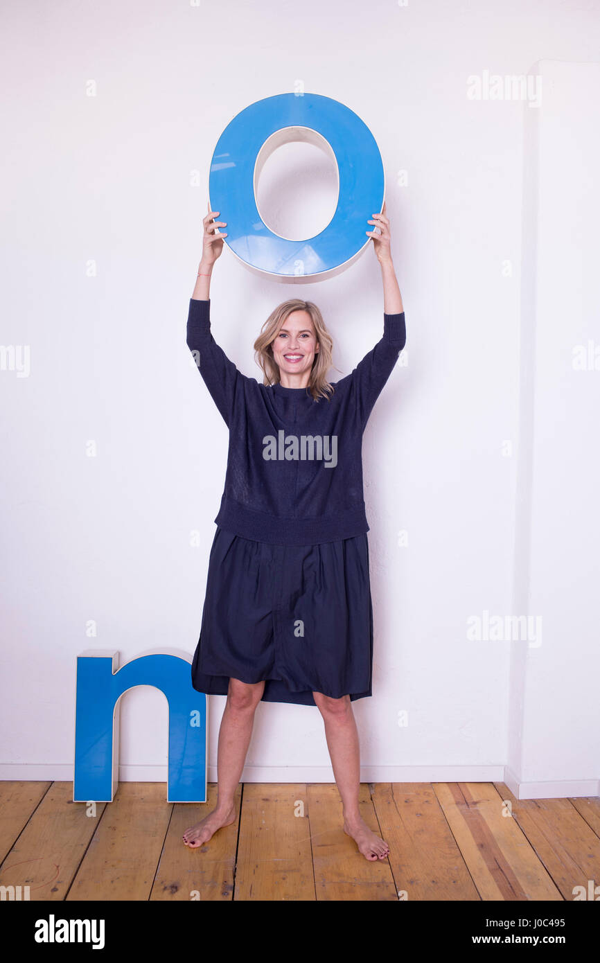 Ritratto di metà donna adulta, tenendo tridimensionale di lettera 'O', accanto alla lettera 'N' sul pavimento Foto Stock