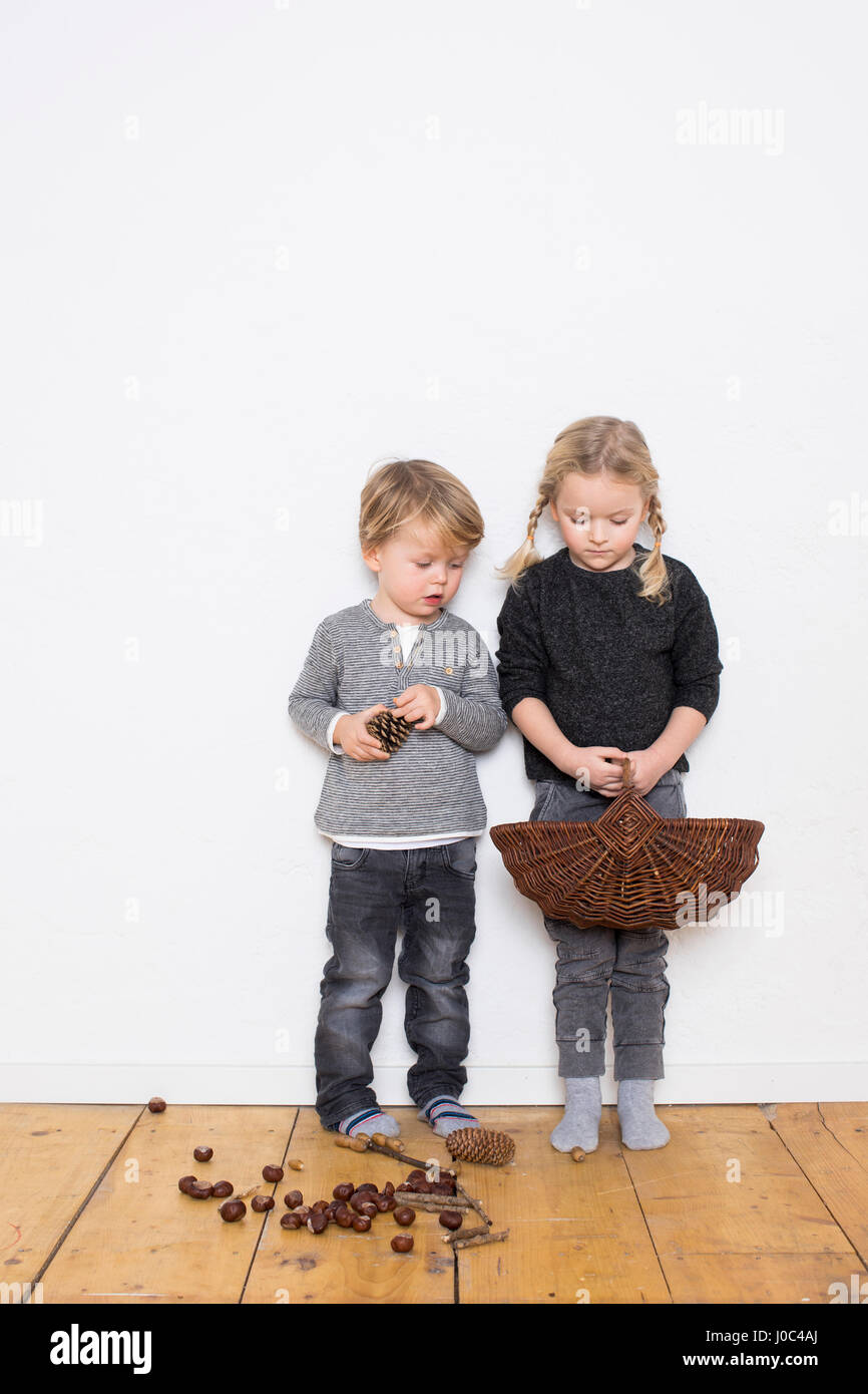 Giovane ragazza e ragazzo e ragazza con cesto in vimini, boy holding pigna, pigne e conkers sul pavimento Foto Stock